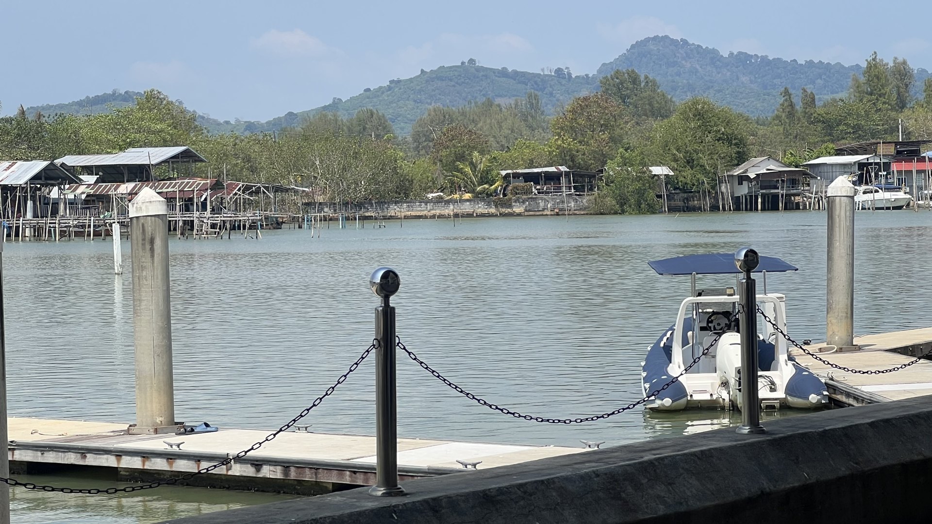 Boats moored beside a waterfront pier with green hills behind
