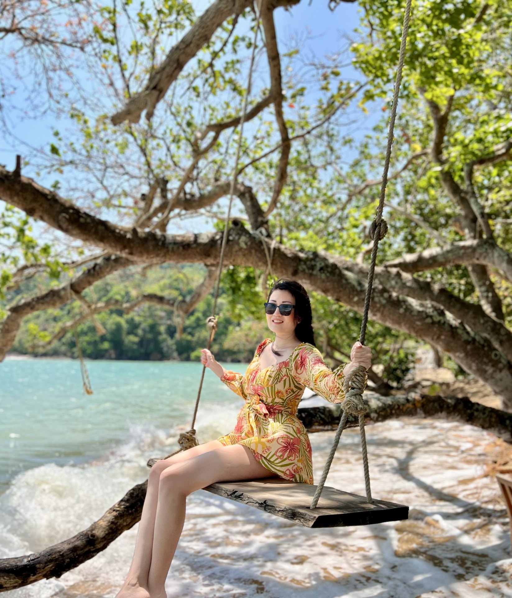 Creator seated on a wooden swing beside turquoise water
