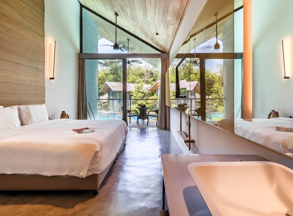 Hotel photograph of a pool-view room with a king bed, high timber ceiling and glass doors facing the pool