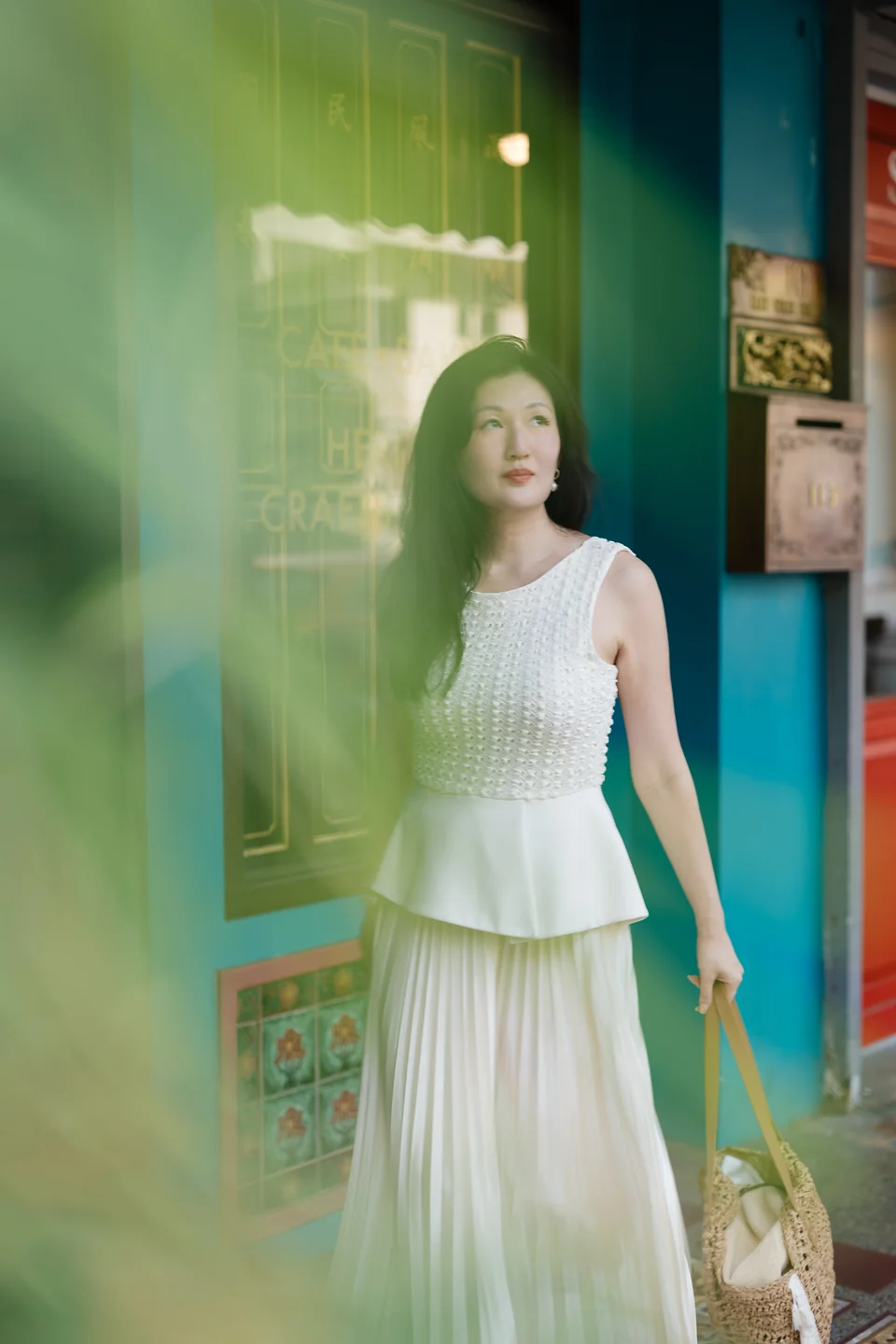 Ki in an ivory outfit outside Rumah Bebe, framed by softly blurred foliage against the turquoise frontage