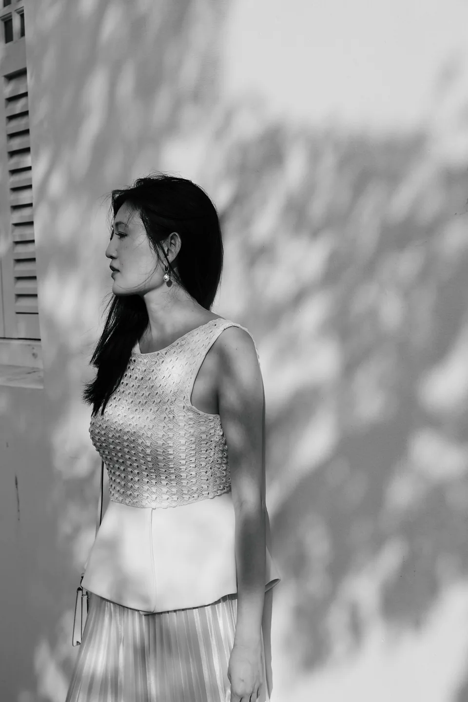 Black-and-white side portrait against a white wall with leaf shadows
